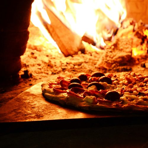 Delicious pizza baking in a traditional wood-fired oven with vibrant flames.