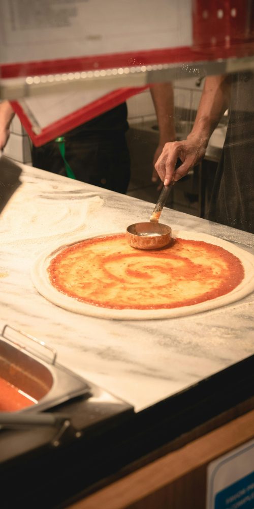 Authentic Italian pizza preparation with fresh tomato sauce on dough in a Brazilian kitchen.