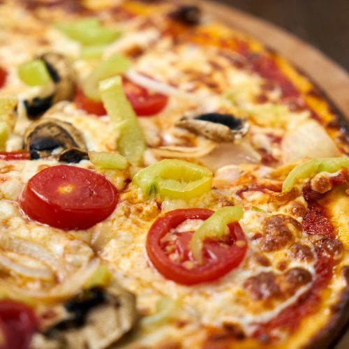 Close-up of a freshly baked Italian pizza topped with vibrant vegetables and cheese.